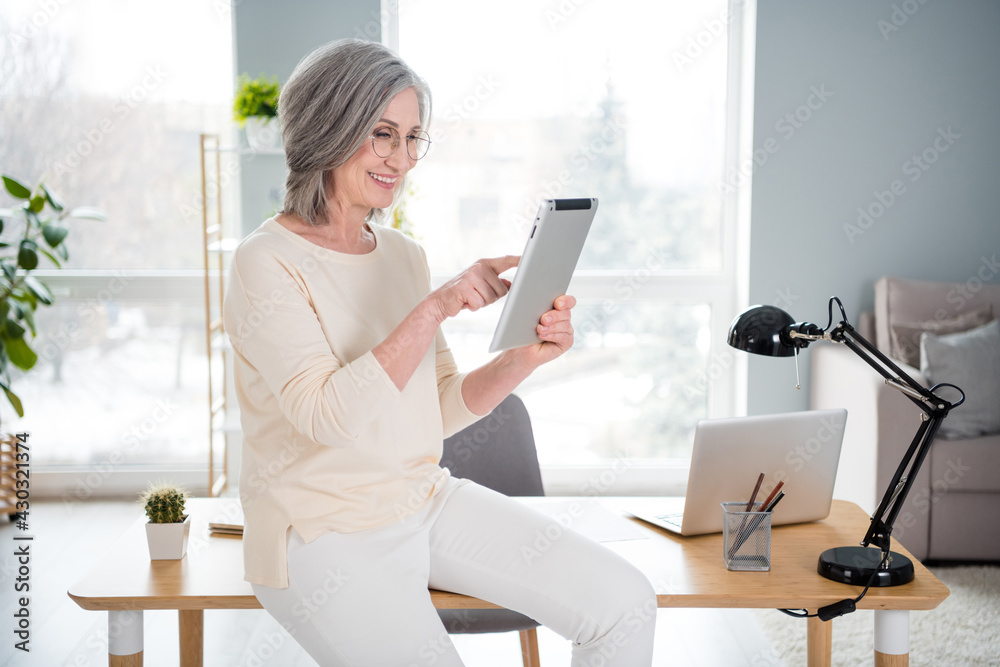 Photo of happy cheerful old woman look hold hand tablet smile office job sit desk indoors inside apartment Photo of happy cheerful old woman look hold hand tablet smile office job sit desk indoors inside apartment