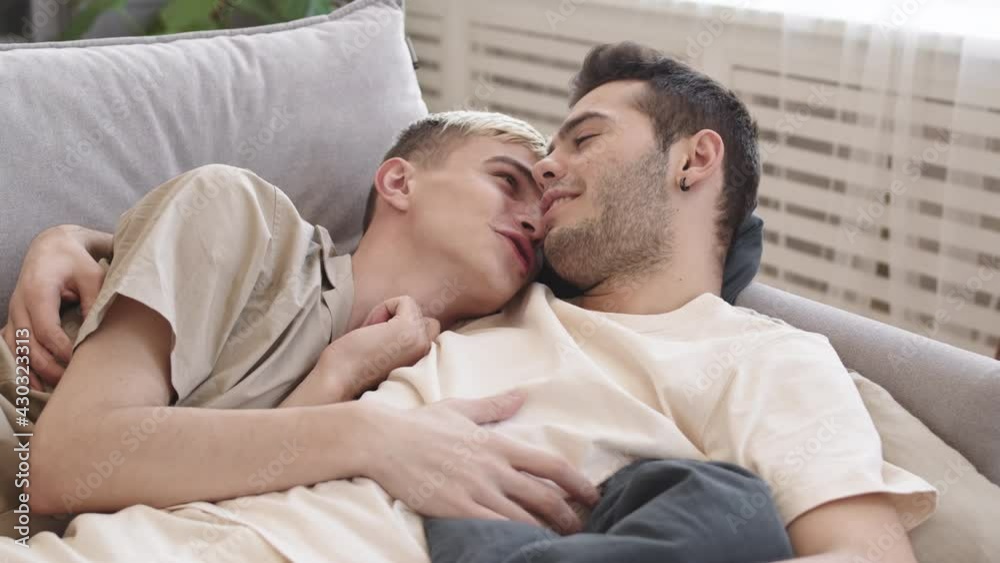 Lockdown of young dark-haired Caucasian man and his beloved boyfriend lying together on sofa at home, hugging, talking and kissing Lockdown of young dark-haired Caucasian man and his beloved boyfriend lying together on sofa at home, hugging, talking and kissing