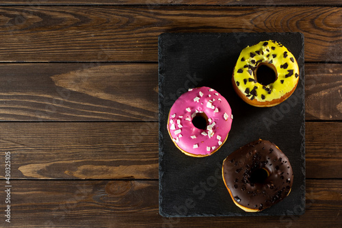 Good morning concept - Freshly baked colorful donuts with cream and pink filling on a wooden table for breakfast. dark background. place for text.