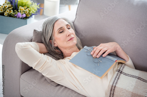 Fotografie Photo of nice sleepy calm old woman relax take nap hold book glasses indoors ins