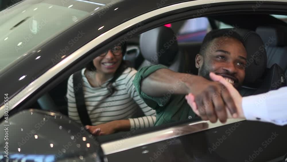 Buy car, african man client in showroom take key sitting in new rental auto with woman, smile Spbd