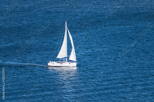 aerial view of a generic white sailboat with two sails sailing on very calm water in the San Diego Bay in Southern California surrounded by small ripples and swells
