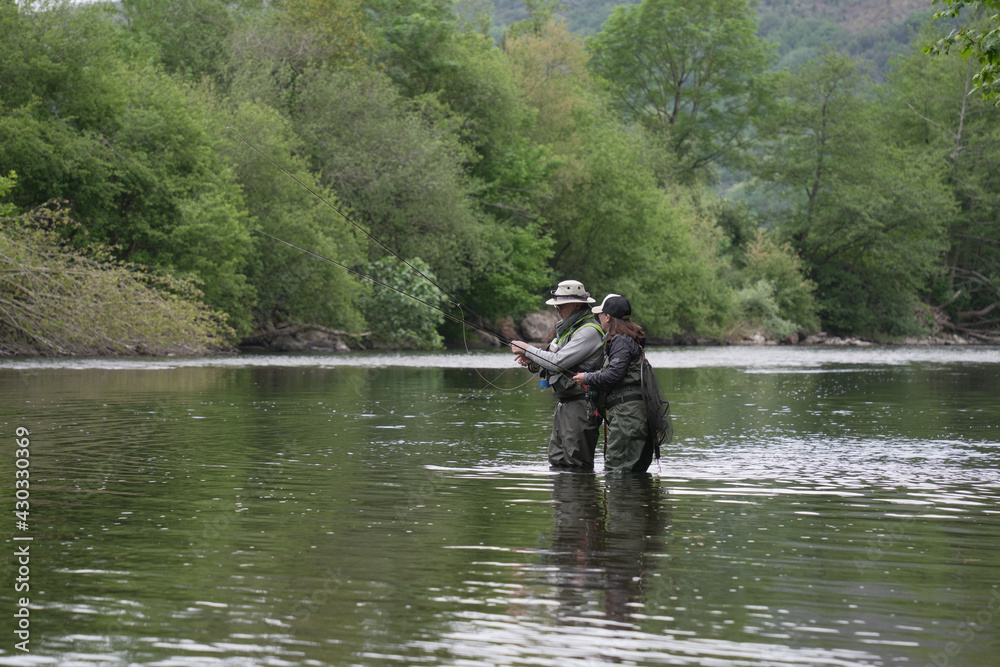 fishing guide with a young woman fly fishing for trout in a clear river fishing guide with a young woman fly fishing for trout in a clear river