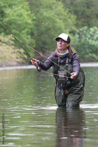 young woman fly fishing for trout in a clear river