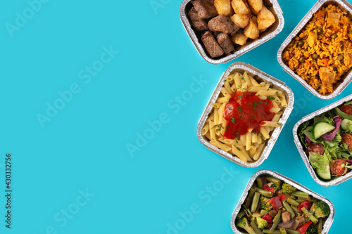 Take away healthy food in foil boxes on blue background. Copy space