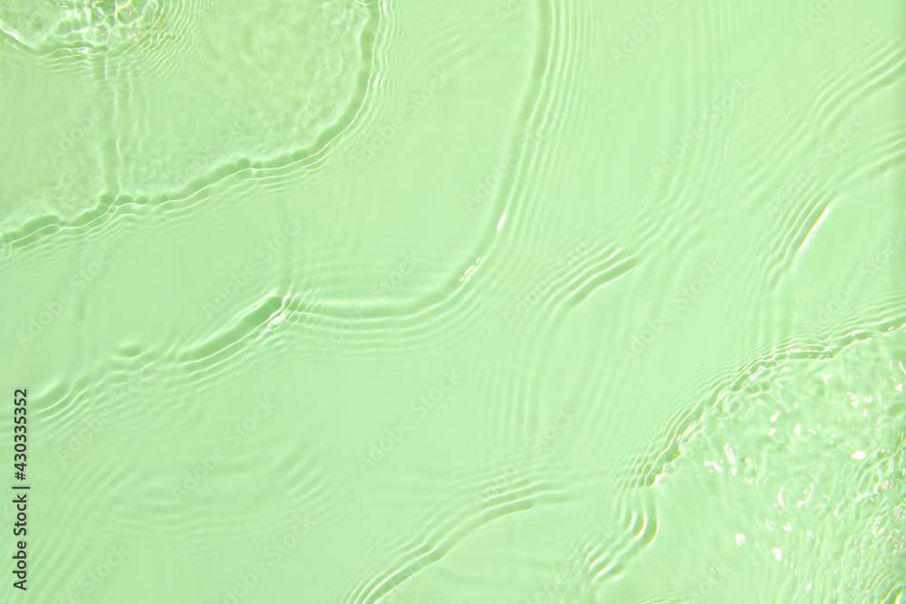 Fototapeta premium De-focused closeup of mint green transparent clear calm water surface texture with splashes and bubbles. Trendy abstract summer nature background. Mint colored waves in sunlight with copy space.
