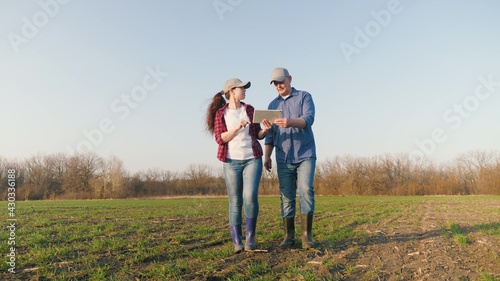 An entrepreneur and an agronomist are studying seedlings of crops in field. Farmers man, woman with tablet computer work in field. Business people teamwork. Smart farming technologies in agriculture