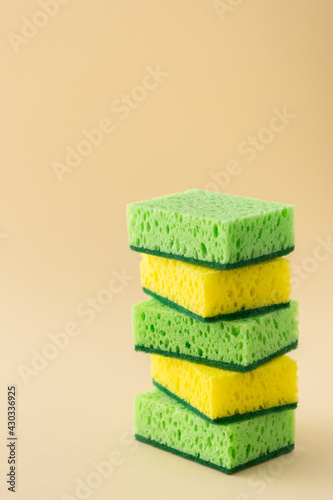Stack of green and yellow dishwashing sponges on neutral beige background, kitchen household and cleaning concept