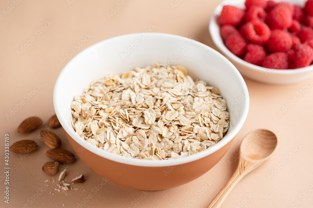 Oat flakes in bowl ready for cooking oatmeal porridge. Oat muesli on beige background. Healthy breakfast cereals food, dieting, fitness food menu concept Oat flakes in bowl ready for cooking oatmeal porridge. Oat muesli on beige background. Healthy breakfast cereals food, dieting, fitness food menu concept