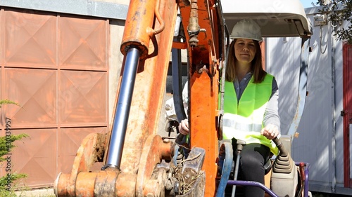 Woman foreman wearing work helmet and reflecting jacket drives an excavator at building site. Working concept.
