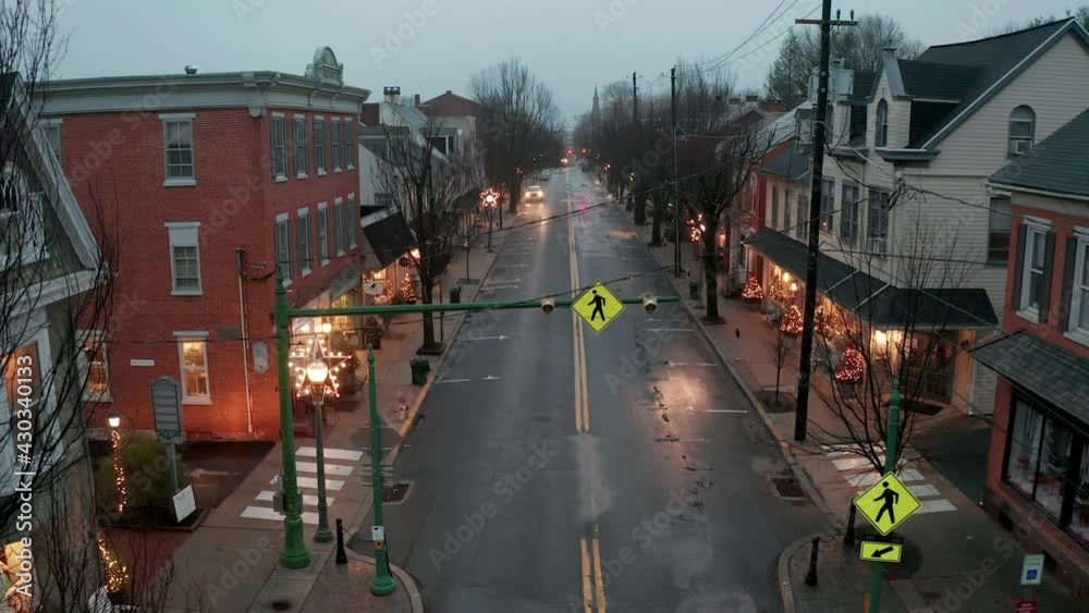 Rising aerial reveals small town America, decorated with Christmas lights. Rainy overcast night shot. Restored stores and buildings on Main Street, Lititz, PA, USA.