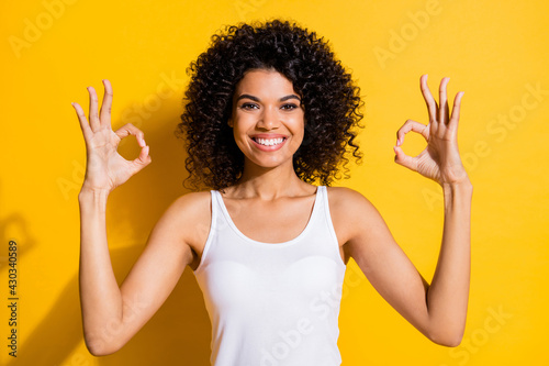 Photo of sweet young dark skin lady wear white singlet showing okey two hands arms isolated yellow color background