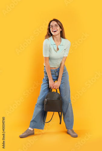 Happy woman with backpack on yellow background