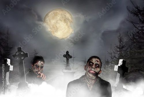 Scary zombies at misty cemetery with old creepy headstones under full moon. Halloween monsters