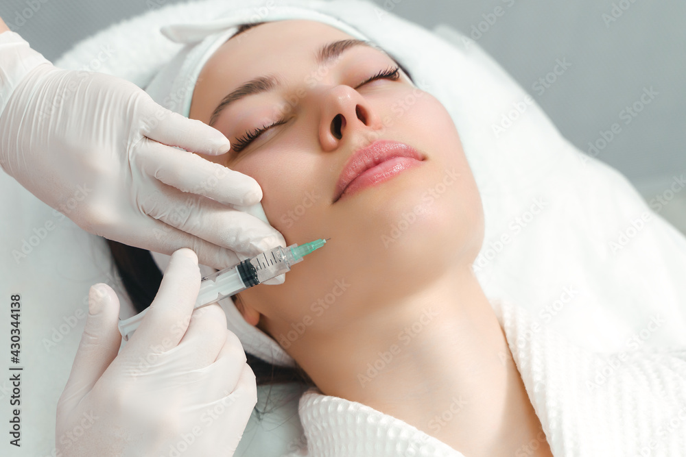 The doctor cosmetologist makes the rejuvenating facial injections procedure for tightening and smoothing wrinkles on the face skin of a beautiful, young woman in a beauty salon. Cosmetology, skincare