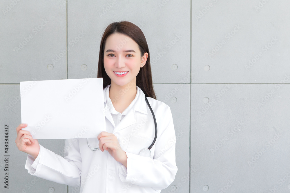 Asian woman doctor who wears medical coat holds and shows white paper to present something in healthcare concept. Asian woman doctor who wears medical coat holds and shows white paper to present something in healthcare concept.