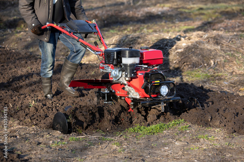 A farmer man plows the land with a cultivator. machinery cultivator for soil cultivation in the garden, motor cultivator.