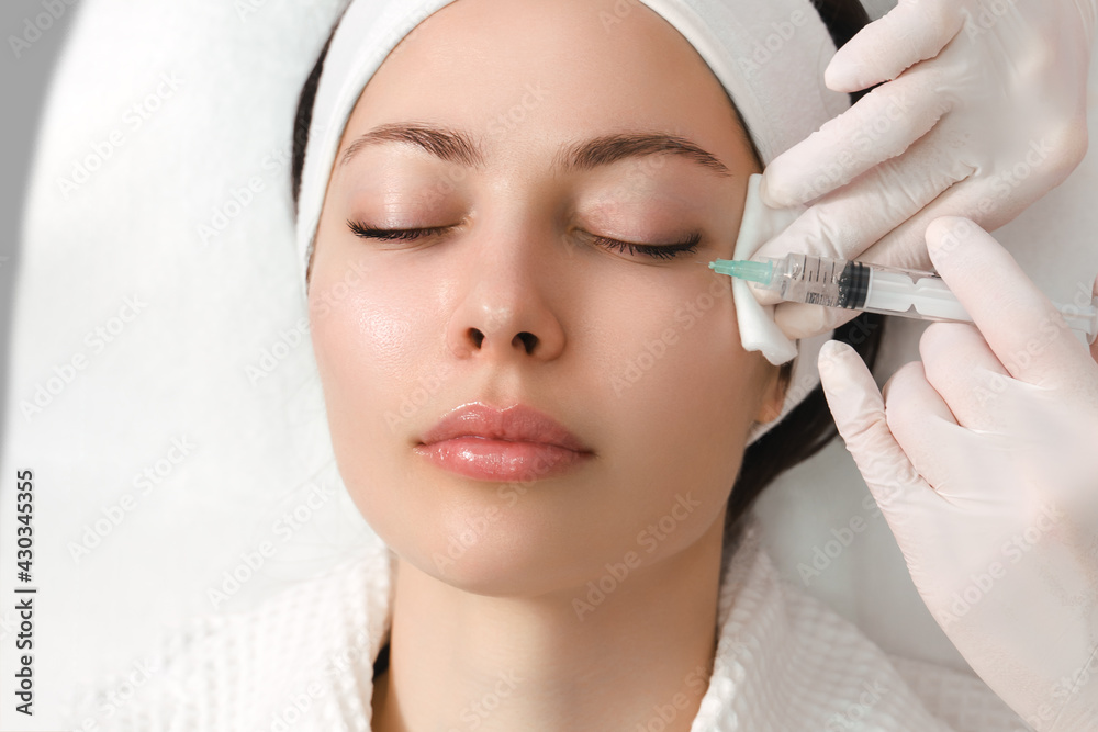 The doctor cosmetologist makes the rejuvenating facial injections procedure for tightening and smoothing wrinkles on the face skin of a beautiful, young woman in a beauty salon. Cosmetology, skincare