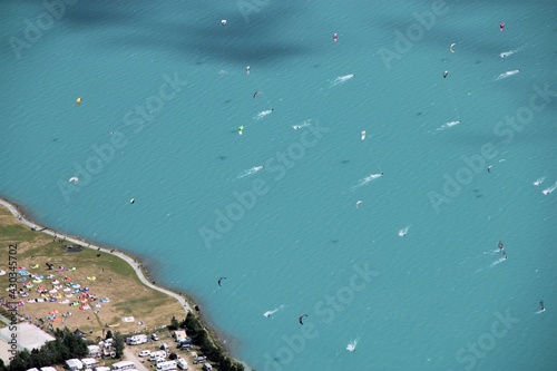 Kitesurfers and windsurfers ploughing through the stark turquoise water of Silvaplana lake, Switzerland, creating lines of foaming whitewater, from above photo