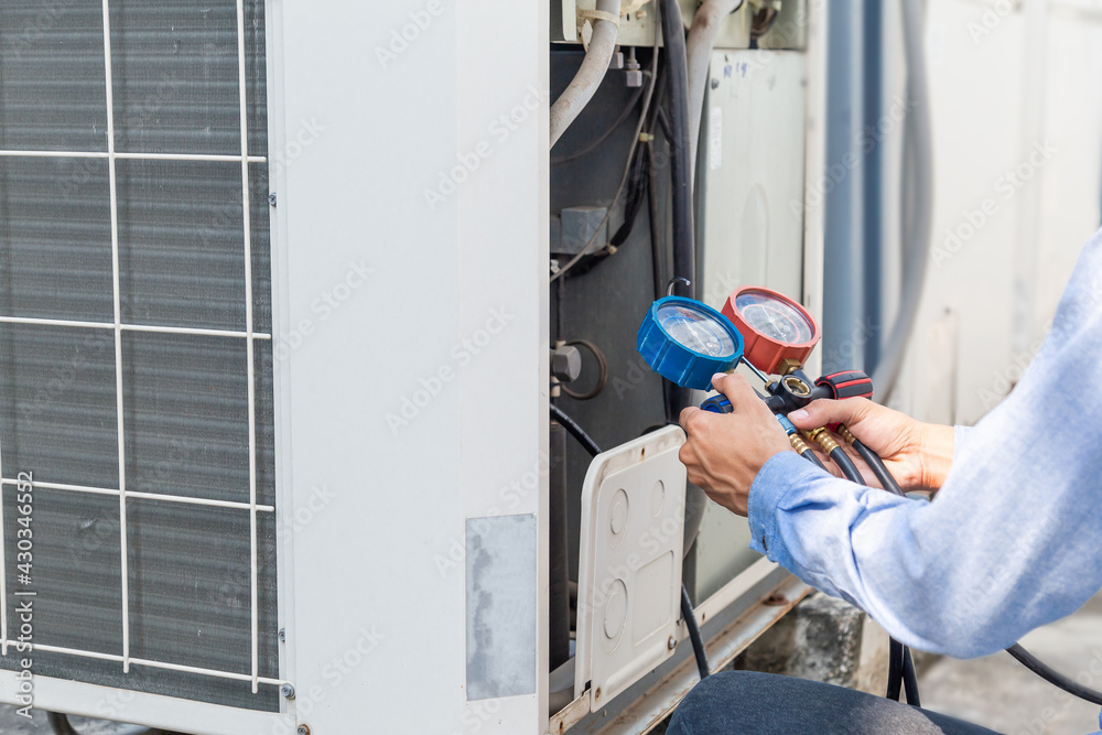 Air repair mechanic using measuring equipment for filling industrial factory air conditioners and checking maintenance outdoor air compressor unit.