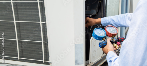 Air repair mechanic using measuring equipment for filling industrial factory air conditioners and checking maintenance outdoor air compressor unit.