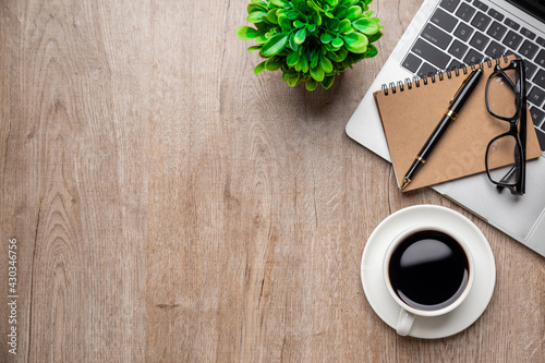 Flat lay, top view office table desk. Workspace with, laptop,office supplies, pencil, green leaf, and coffee cup on wood background.