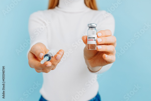 Young woman holding covid-19 vaccine bottle, doctor in laboratory with biological test tube on blue background