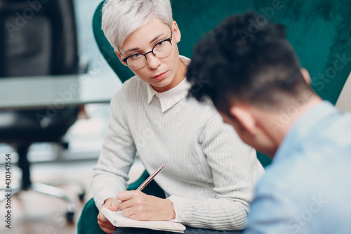 Woman with pen and notebook in hand writes and man sitting on chair together.  Journalism, interview and HR recruitment survey contract concept human resources