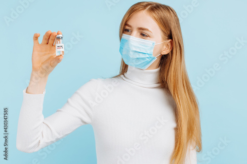 Doctor holding a vial with a dose of covid 19 corona virus vaccine for injection, on a blue background