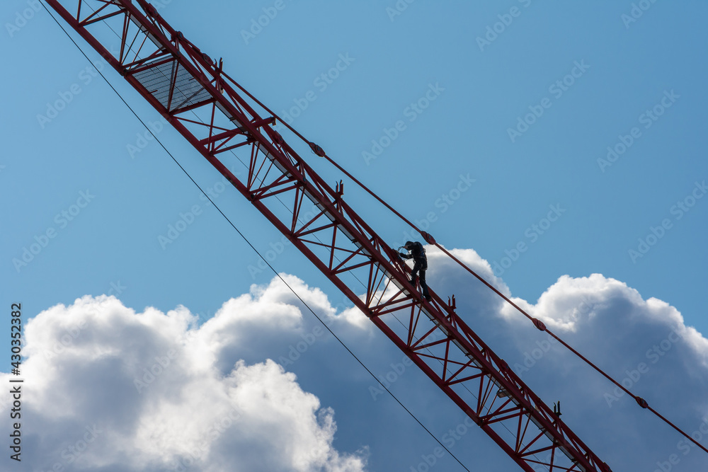High-rise worker on a crane boom against the background of clouds