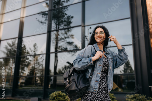 Happy young woman walking on city streets with a leather backpack, smiling.