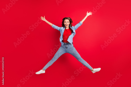 Photo of shiny adorable young woman wear jeans shirt smiling jumping high like star isolated red color background