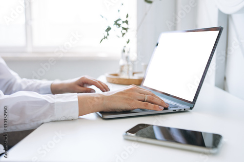 Crop photo of young woman in white shirt working on laptop with the white screen on table  mockup