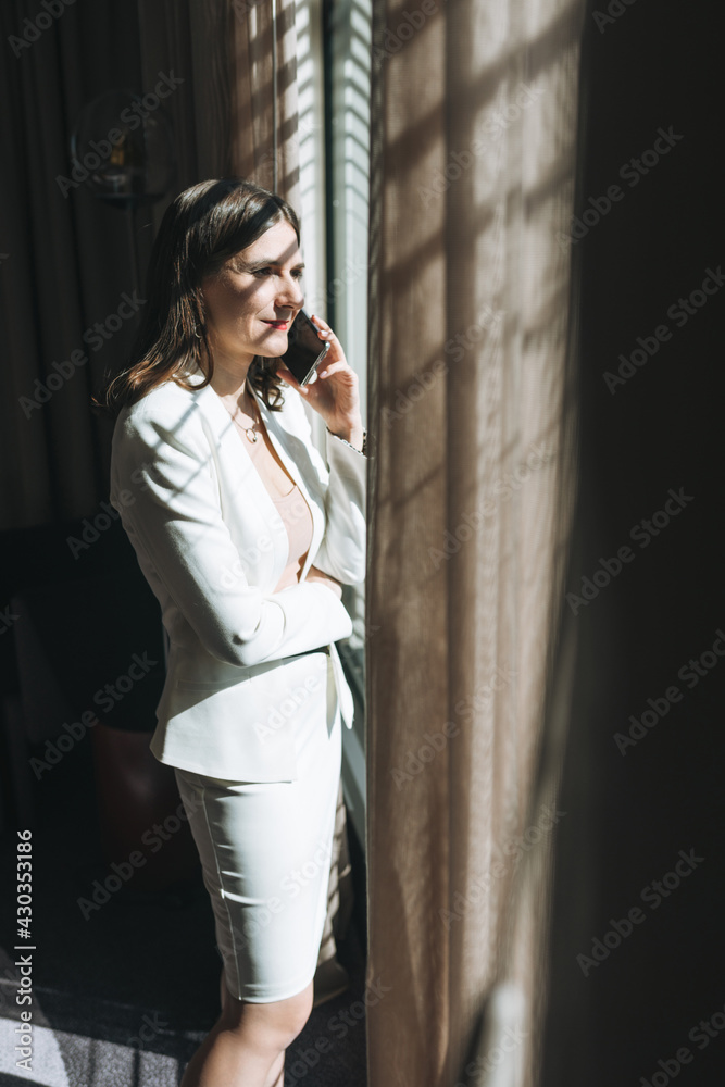 Young brunette woman business lady in white suit with mobile in hotel room Young brunette woman business lady in white suit with mobile in hotel room