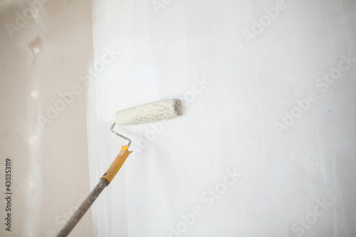 White paint roller in hand with drywall wall painting.