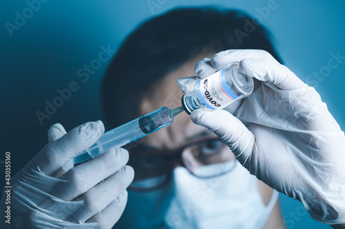 A man s hand wearing medical gloves. Using a cyring inserted into a covid-19 vaccine bottle against a blurry background.