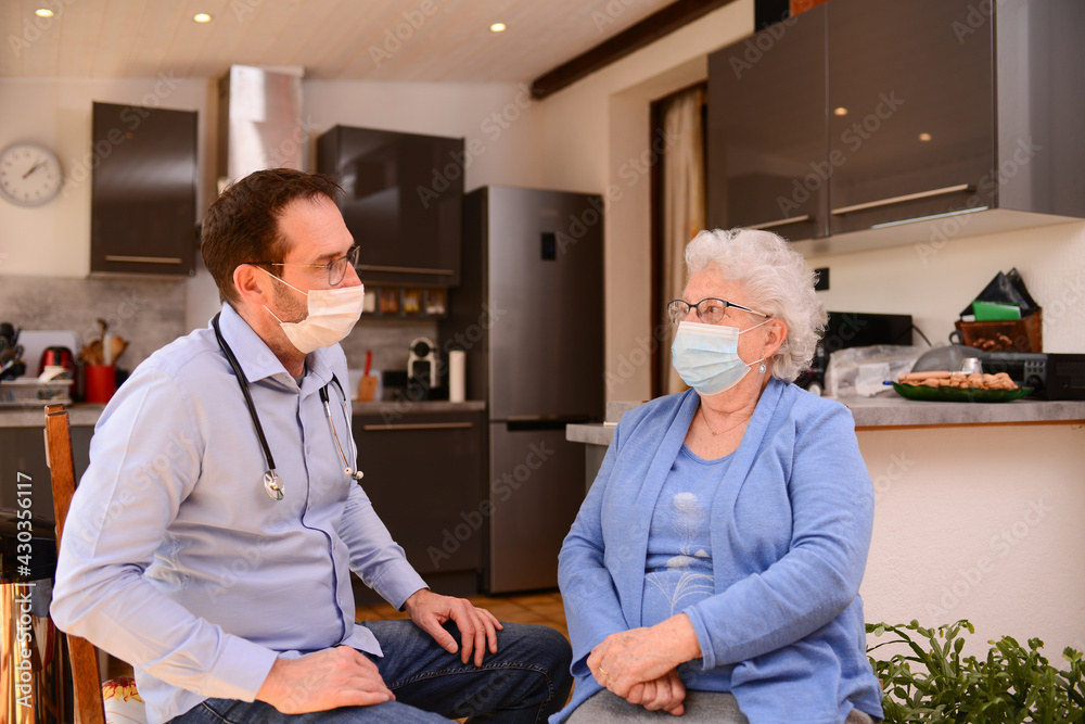Obraz premium young male doctor checking medical exam consultation to an elderly senior woman at home wearing surgical mask to avoid covid 19 contamination