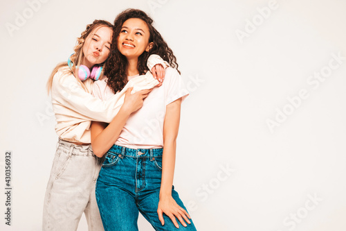 Two young beautiful smiling international hipster female in trendy summer clothes.Sexy carefree women posing on grey background in studio.Positive models having fun.Concept of friendship