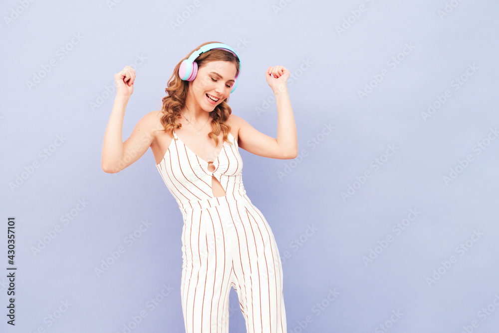Beautiful smiling woman dressed in summer clothes. Sexy carefree model listening music in wireless headphones. Adorable and positive female posing near purple wall in studio.Dancing Beautiful smiling woman dressed in summer clothes. Sexy carefree model listening music in wireless headphones. Adorable and positive female posing near purple wall in studio.Dancing