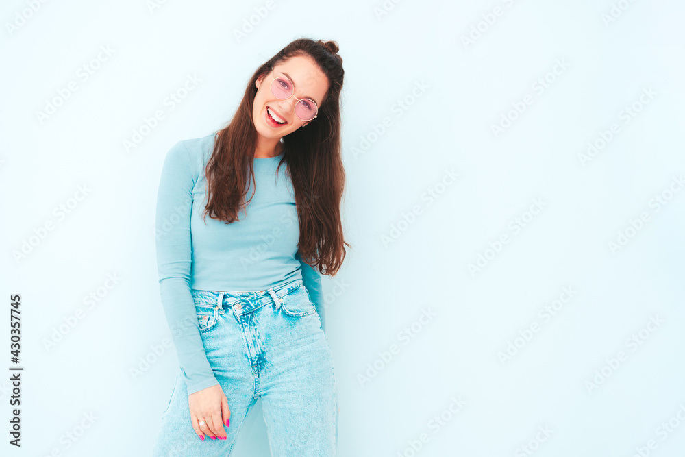 Young beautiful smiling female in trendy summer hipster clothes. Sexy carefree woman posing near light blue wall in studio. Positive model having fun indoors. Cheerful and happy Young beautiful smiling female in trendy summer hipster clothes. Sexy carefree woman posing near light blue wall in studio. Positive model having fun indoors. Cheerful and happy