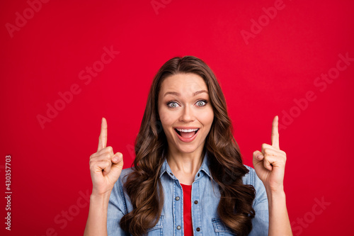 Portrait of attractive amazed cheerful wavy-haired girl demonstrating up ad offer isolated over vibrant red color background