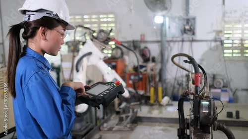 Asian factory worker woman control industrial robot arm machine by using the controller box and she inspect function of machine. Management and support system for industrial business concept. 
