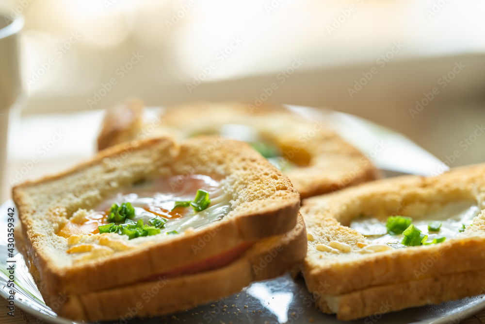 Morning breakfast. Fragrant baked sandwiches with egg, ham, cheese and pickles lie on a plate on the table, next to a mug of green tea in the kitchen on the table with morning sunlight.
