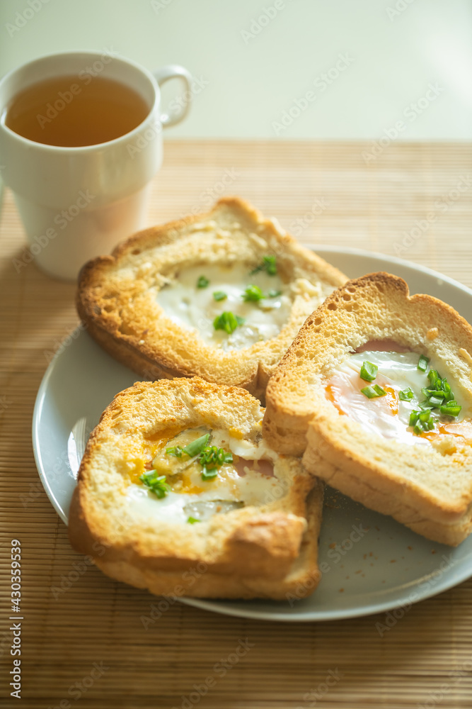 Morning breakfast. Fragrant baked sandwiches with egg, ham, cheese and pickles lie on a plate on the table, next to a mug of green tea in the kitchen on the table with morning sunlight. Morning breakfast. Fragrant baked sandwiches with egg, ham, cheese and pickles lie on a plate on the table, next to a mug of green tea in the kitchen on the table with morning sunlight.