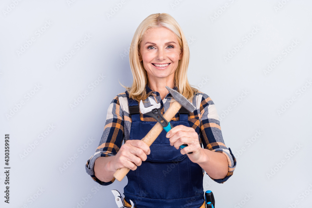 Photo of positive adorable age crafts lady dressed blue uniform smiling holding tools crossed isolated grey color background Photo of positive adorable age crafts lady dressed blue uniform smiling holding tools crossed isolated grey color background