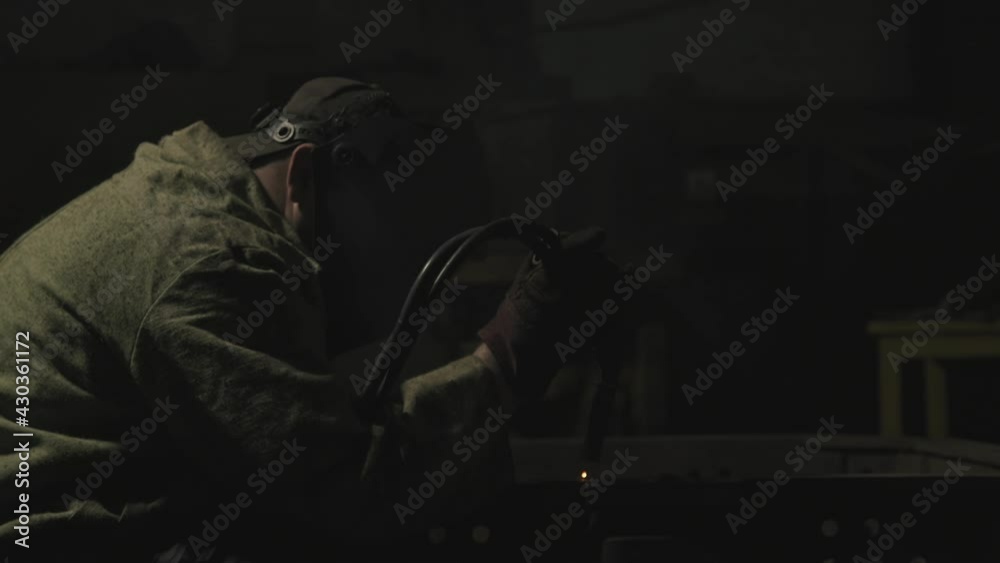 Side-view medium shot of unrecognizable man working as welder doing his job welding steel and other metals at tractor plant Side-view medium shot of unrecognizable man working as welder doing his job welding steel and other metals at tractor plant