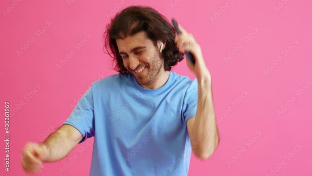 The happy man in headphones dancing with the phone in hands in the pink studio The happy man in headphones dancing with the phone in hands in the pink studio