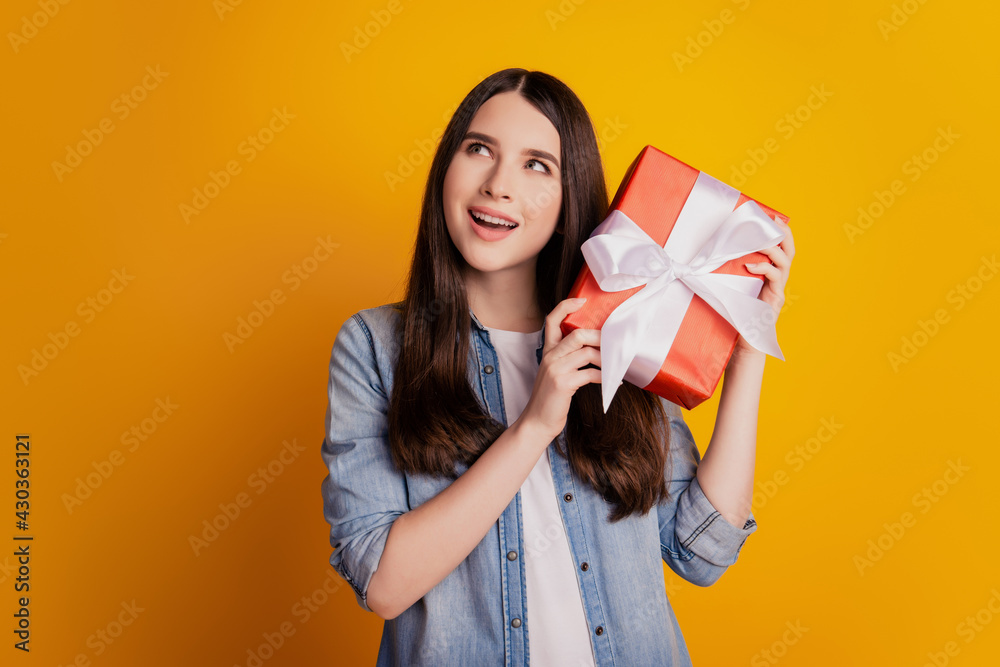 Portrait of dreamy curious girl hold present box guessing look empty space on yellow background Portrait of dreamy curious girl hold present box guessing look empty space on yellow background