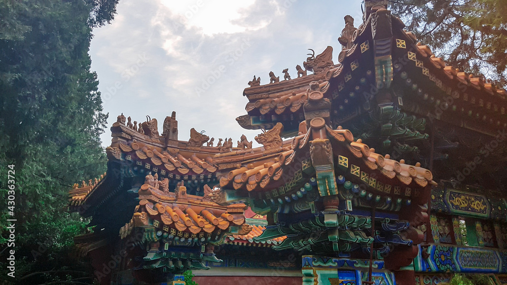 Naklejka premium A close up on a massive pavilion inside of Jingshan Park in Beijing, China. The buildings have very richly decorated rooftops, with elements of gold. Lots of trees around. Chinese architecture