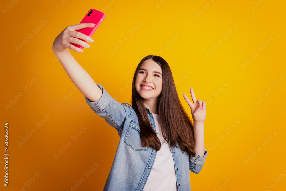 Portrait of charming positive girl holding in hands cell phone take selfie show v-sign Portrait of charming positive girl holding in hands cell phone take selfie show v-sign